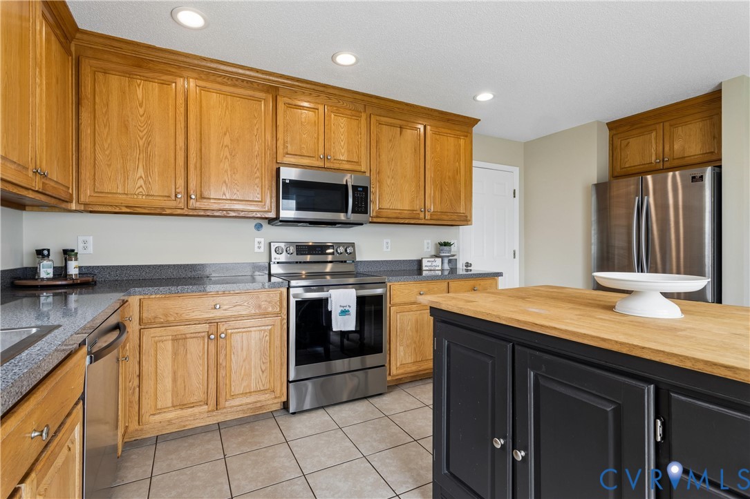 Kitchen featuring wood cabinetry, stainless steel appliances, recessed lighting, a butcher block island, and tile flooring
