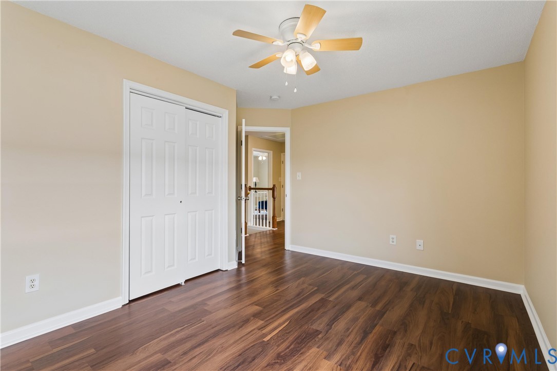Spacious room featuring wood-finish flooring, light tan walls, and a white ceiling fan with light fixture