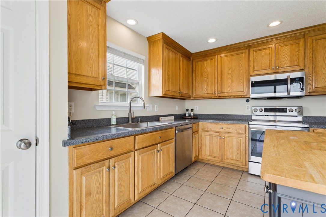 Kitchen featuring extensive wood cabinetry, stainless steel appliances, a stainless steel sink with a gooseneck faucet, dark countertops, and square tile flooring