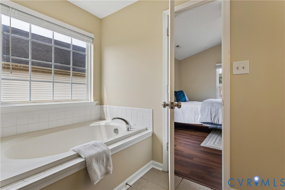 Built-in soaking tub with chrome fixtures, set against a tiled surround and a large window with horizontal blinds