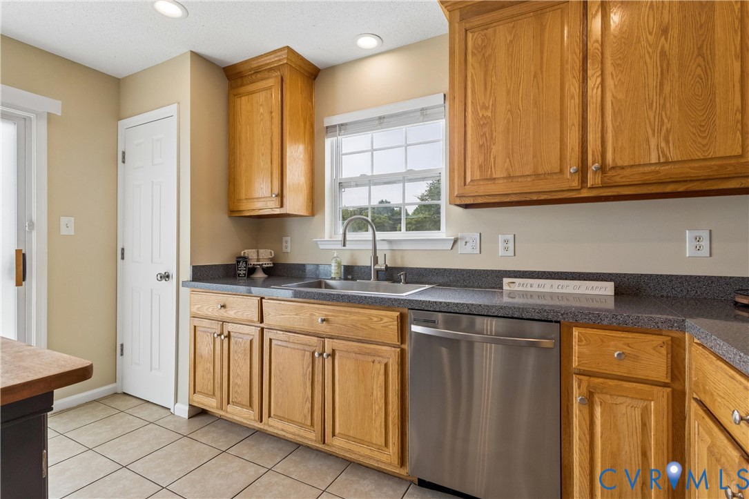 Kitchen featuring wood cabinetry, dark speckled countertops, a stainless steel dishwasher, and a stainless steel sink with a gooseneck faucet