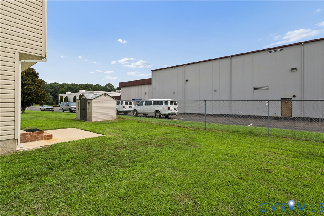 Green lawn area featuring a concrete patio with a brick-built element, a detached storage shed, and a chain-link fence