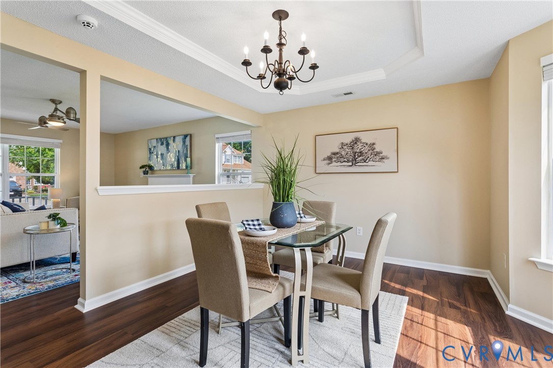 Dining area featuring wood-finish flooring, a tray ceiling with a chandelier, and a pass-through window to an additional living space