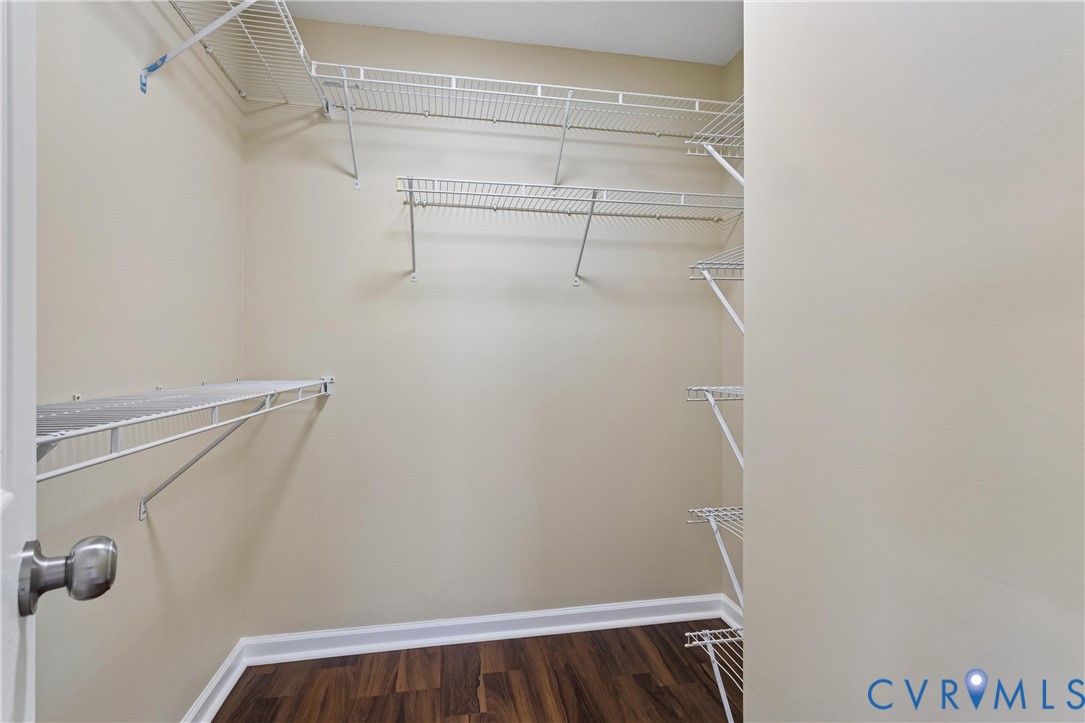 Spacious walk-in closet featuring multiple white wire shelving units and rich wood-finish flooring