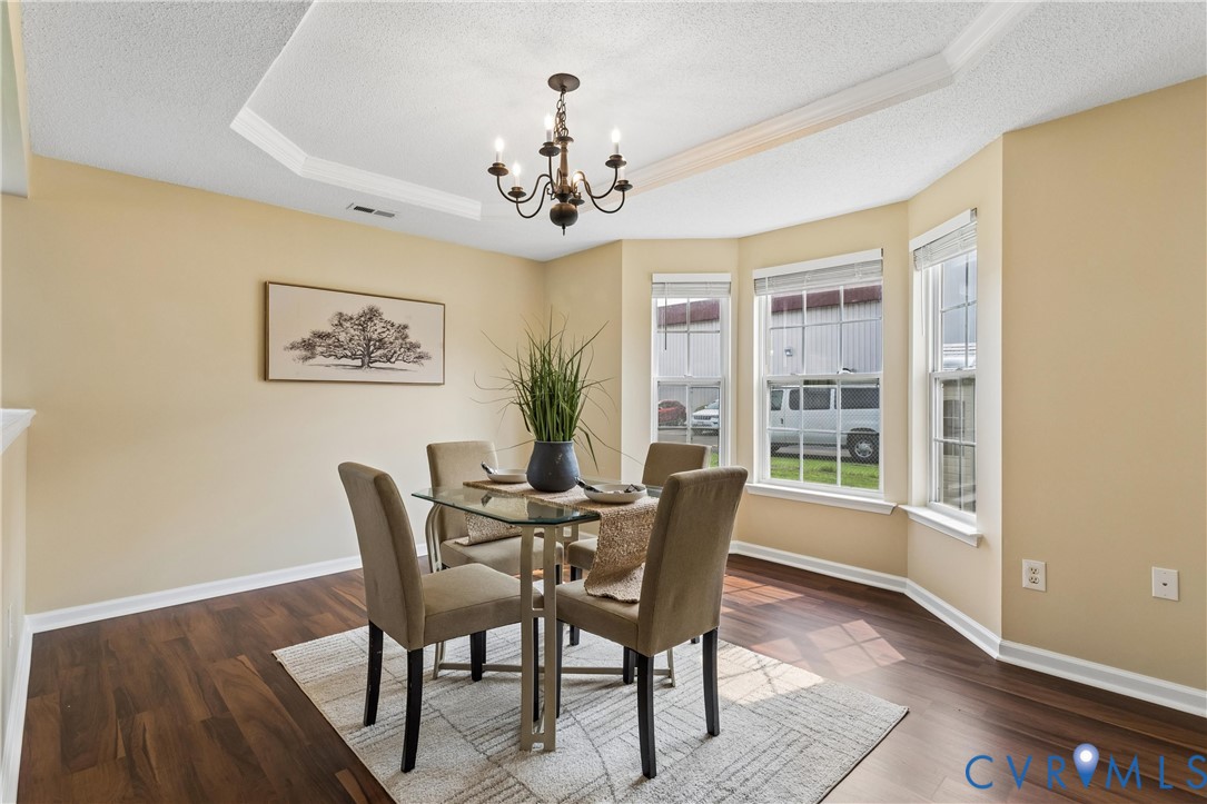 Tray ceiling with crown molding, wood-finish flooring, a bay window with three vertical windows, and a chandelier lighting fixture Tray ceiling with crown molding, wood-finish flooring, a bay window with three vertical windows, and a chandelier lighting fixture