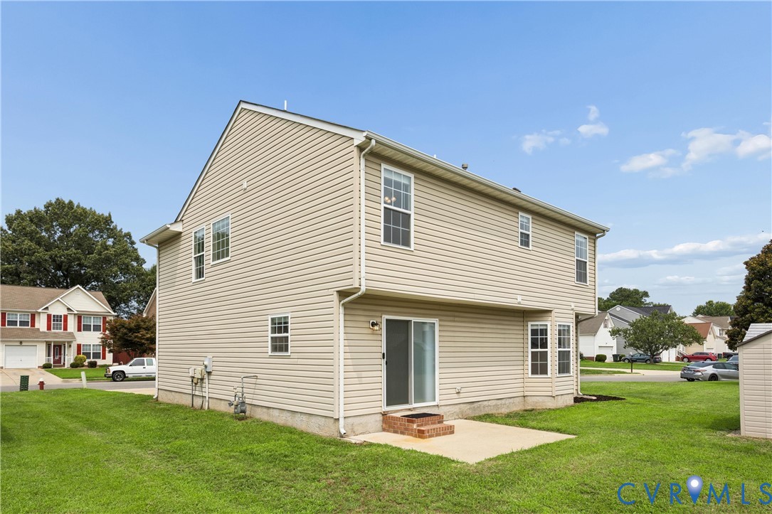 Two-story residence featuring light-colored siding, a concrete patio, and a sliding glass door