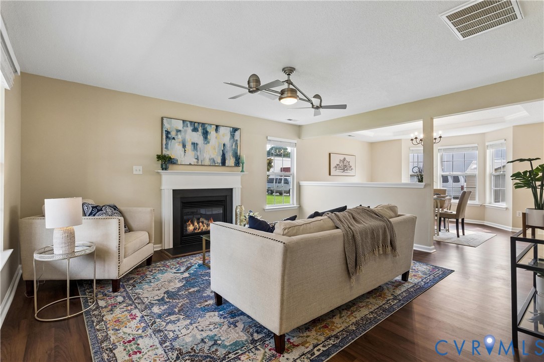 Living room featuring wood-finish flooring, a contemporary ceiling fan, and a fireplace with a white mantel Living room featuring wood-finish flooring, a contemporary ceiling fan, and a fireplace with a white mantel
