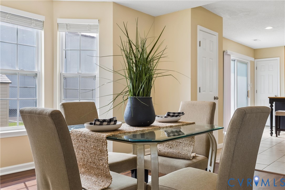 Dining area featuring a glass-top table, hard-surface flooring, multiple windows with blinds, and a paneled door Dining area featuring a glass-top table, hard-surface flooring, multiple windows with blinds, and a paneled door
