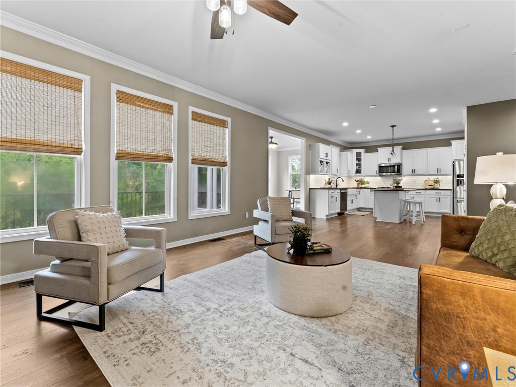 Open-concept living area featuring wood-finish flooring, a ceiling fan, and crown molding