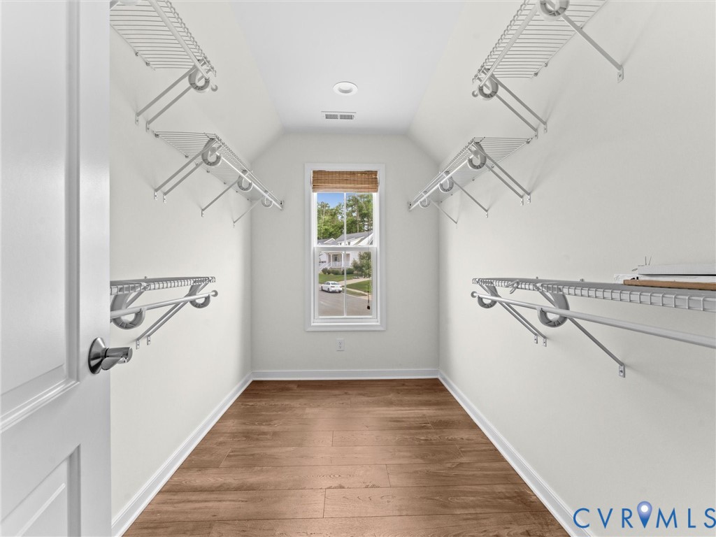 Walk-in closet featuring wood-finish flooring, white walls, multiple wire shelving units, and a window with a woven shade