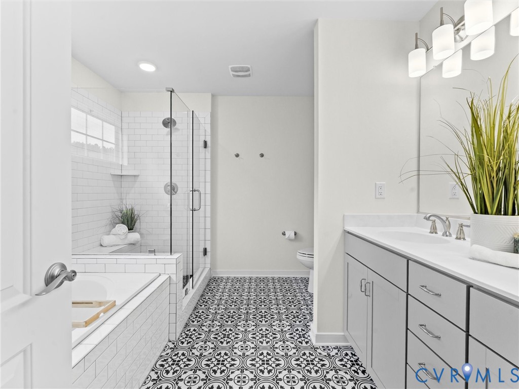 Bathroom featuring patterned floor tiles, a glass-enclosed shower with subway tile surround, a separate soaking tub, and a double vanity with a broad mirror