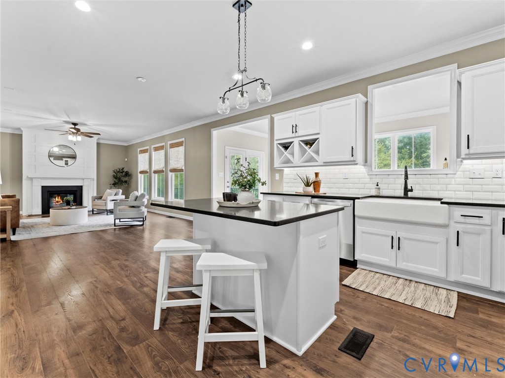 Contemporary kitchen featuring an island with seating, white shaker-style cabinetry, a white farmhouse sink, subway tile backsplash, and dark countertops