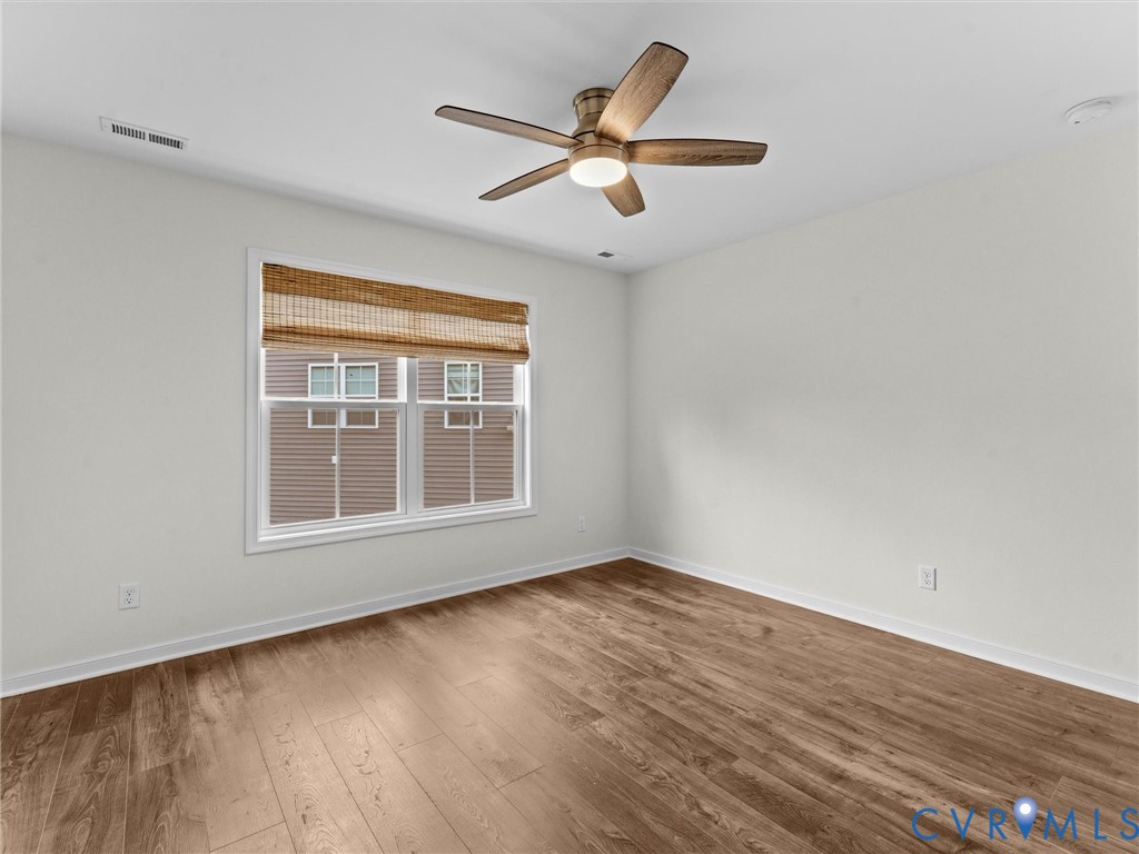 Interior room featuring wood-finish flooring, a ceiling fan with integrated lighting, and a window with a woven shade