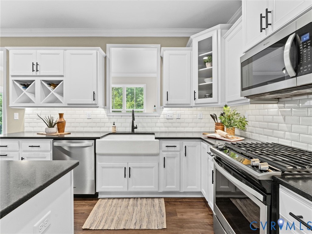 Bright kitchen featuring white shaker cabinetry, black countertops, stainless steel appliances, a farmhouse sink, and subway tile backsplash