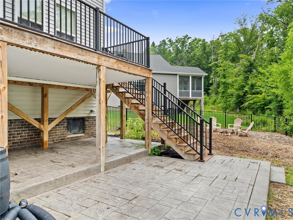 Lower-level stamped concrete patio with direct deck access via exterior staircase, featuring a screened porch, and a fenced perimeter