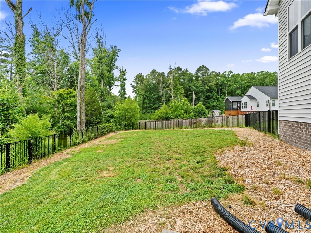Spacious backyard featuring a sloped lawn, black metal fencing, and dense perimeter trees