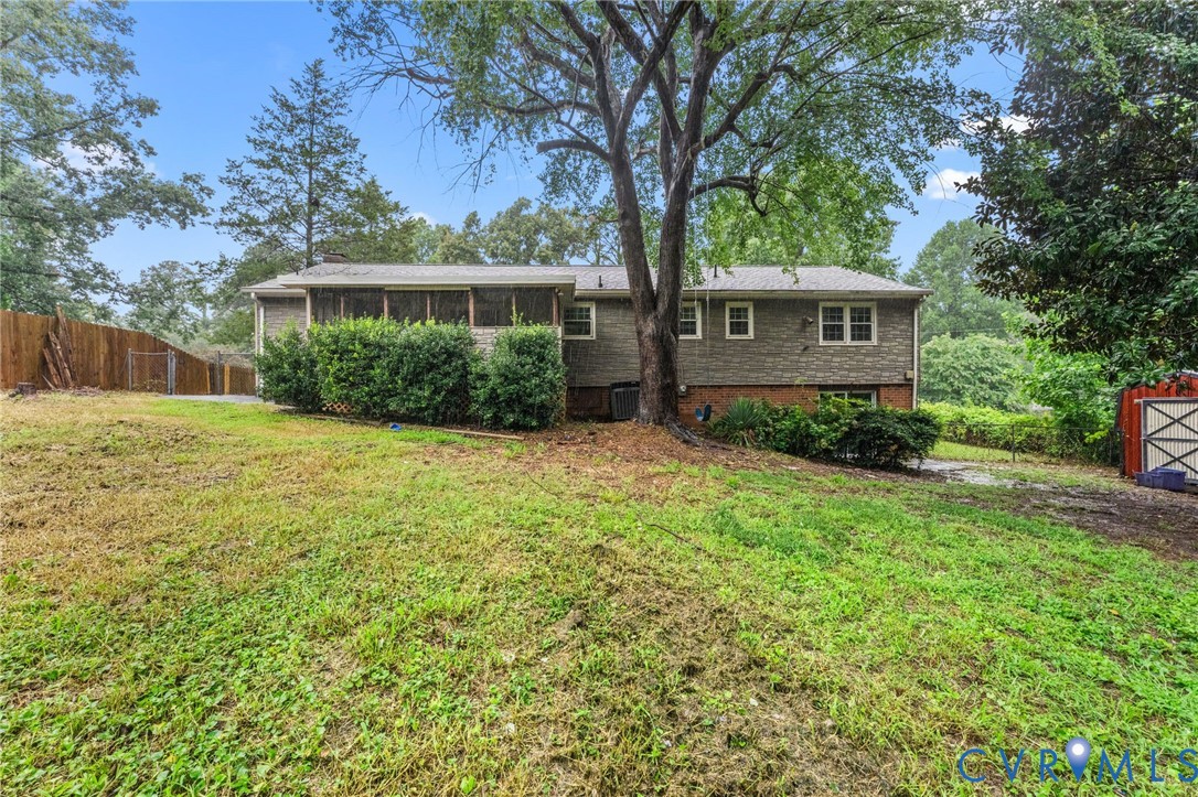 Expansive backyard featuring mature trees, a screened-in porch, privacy fencing, and exterior siding with brick detailing Expansive backyard featuring mature trees, a screened-in porch, privacy fencing, and exterior siding with brick detailing