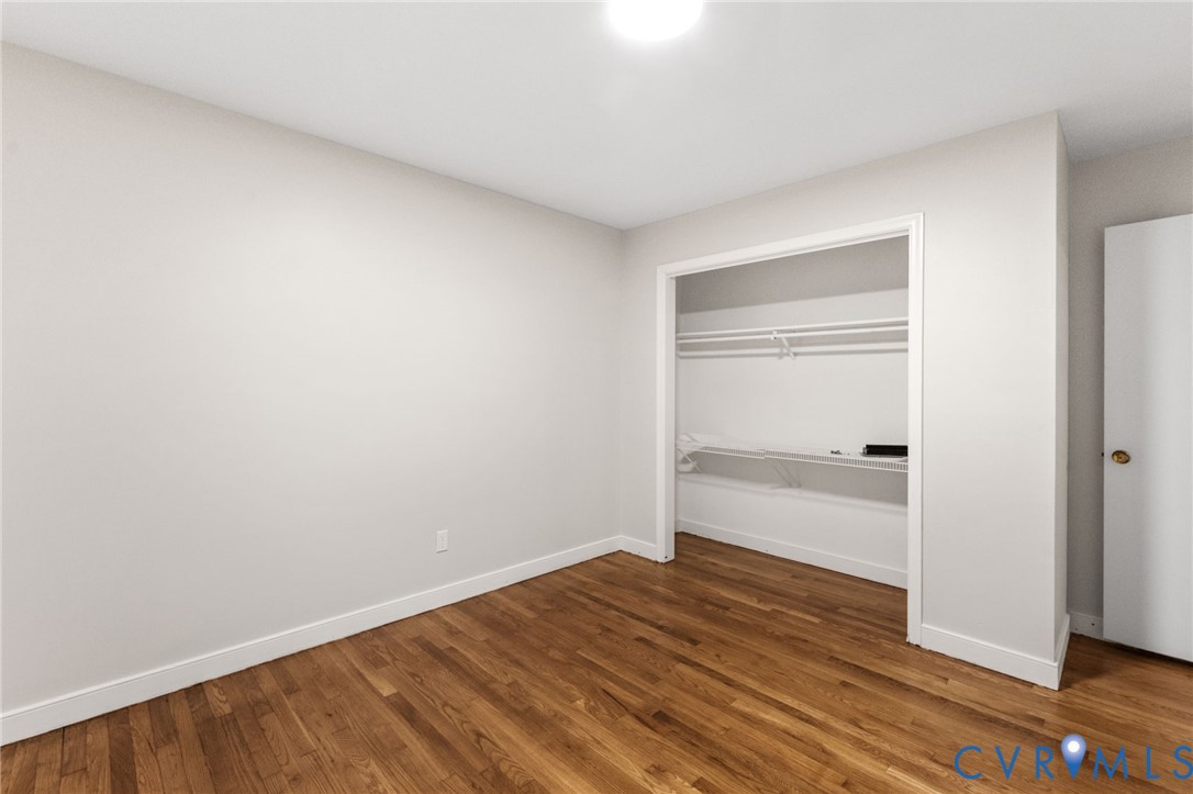 Bright interior space featuring wood-finish flooring, white baseboards, and a built-in closet with shelving and hanging rods