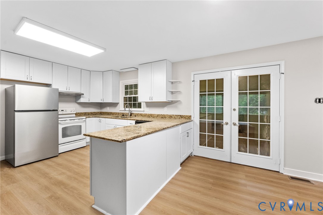 Kitchen featuring white cabinetry, light-toned countertops, a stainless steel refrigerator, a white range, and wood-finish flooring
