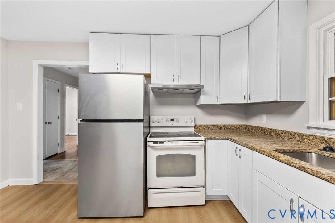 Kitchen featuring light wood-finish flooring, white cabinetry, a stainless steel refrigerator, white electric range with vent hood, and stone-look countertops with an integrated sink