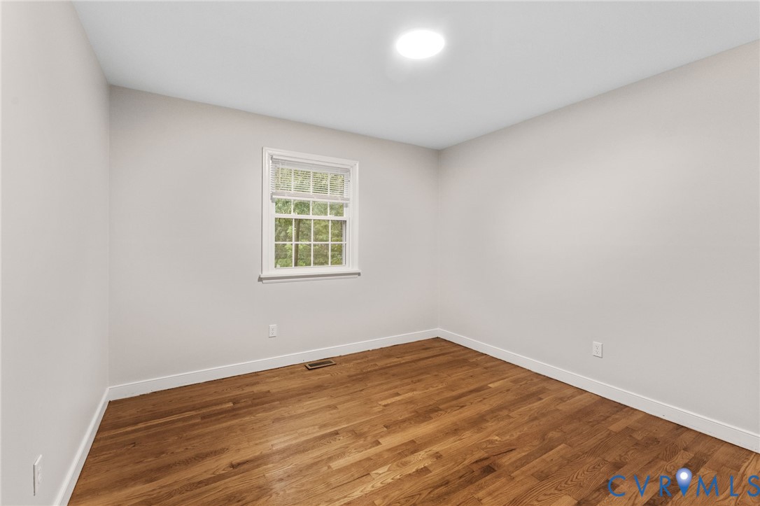 Bright room featuring wood-finish flooring, light-toned wall paint, a double-hung window with white trim, and a ceiling-mounted light fixture