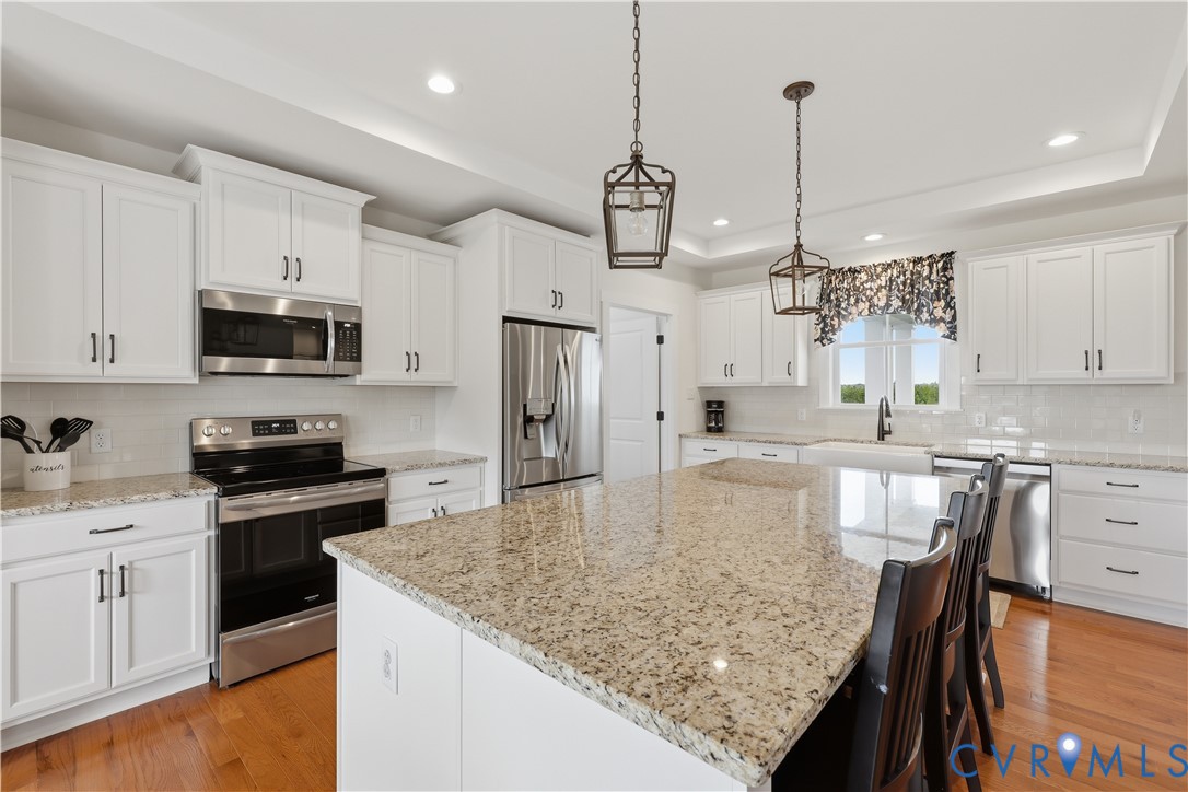 Spacious kitchen featuring an expansive island with granite countertops, white cabinetry, stainless steel appliances, and wood-finish flooring