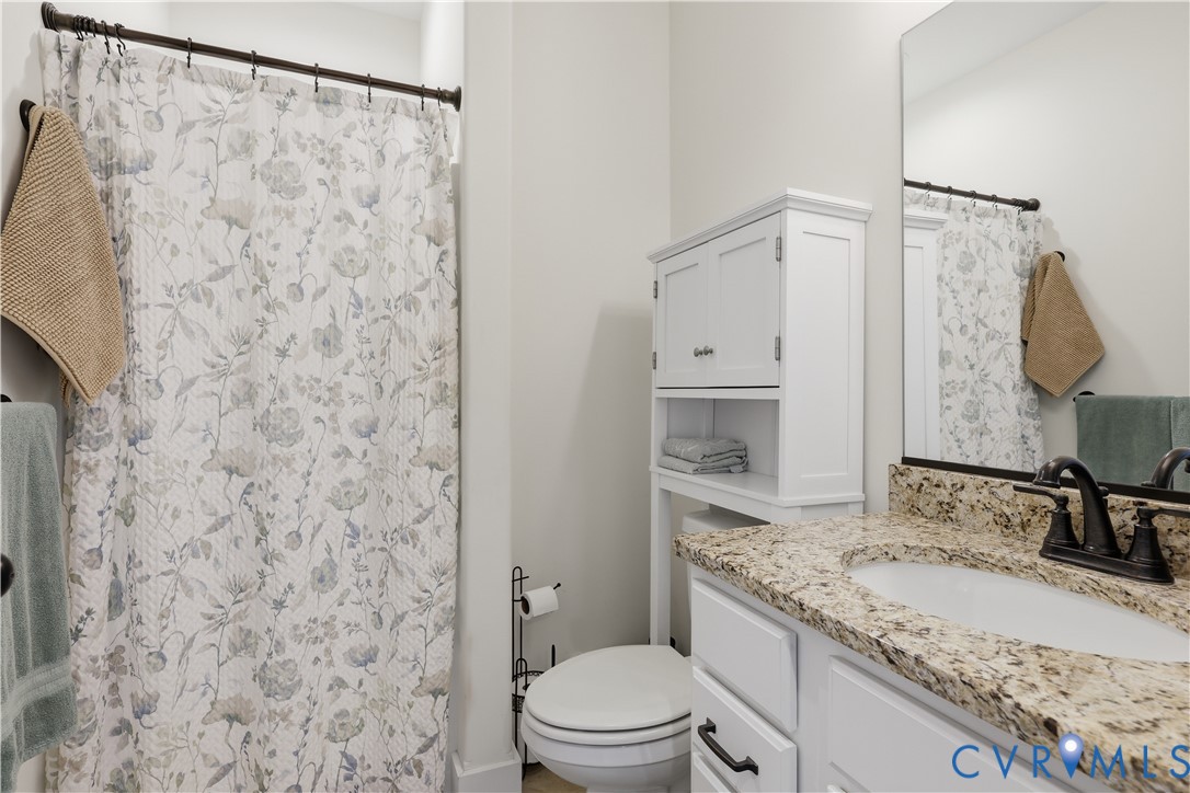 Bathroom featuring a vanity with a granite-style countertop, white cabinetry, undermount sink, and dark bronze-tone faucet
