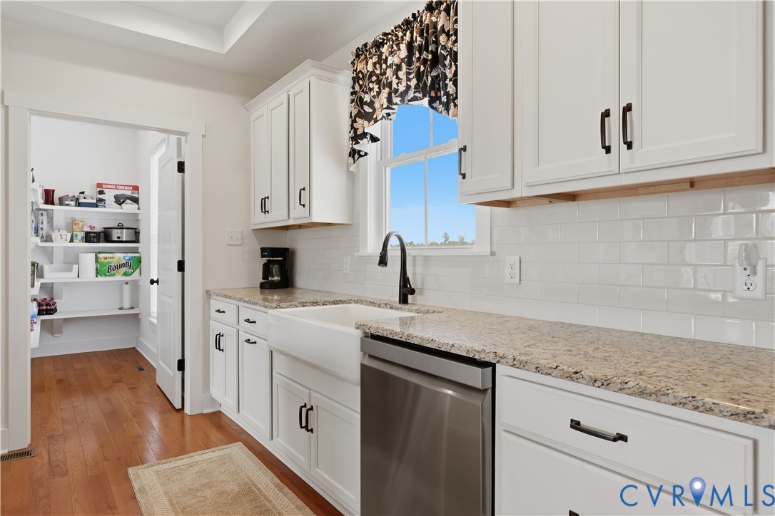 White shaker cabinetry with black hardware, stone-finish countertops, subway tile backsplash, and stainless steel appliances
