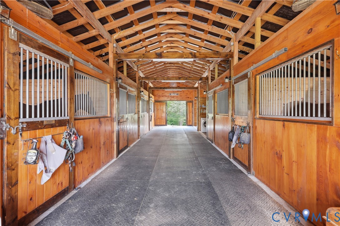 Barn interior featuring multiple stalls with wood paneling and metal grating, exposed wood beam ceiling, and durable textured flooring