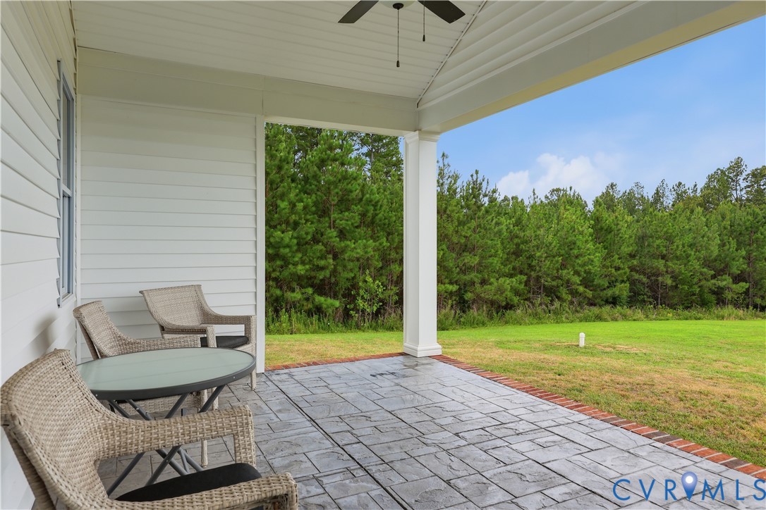 Covered patio featuring stamped concrete flooring, brick edging, a ceiling fan, and a view of mature trees