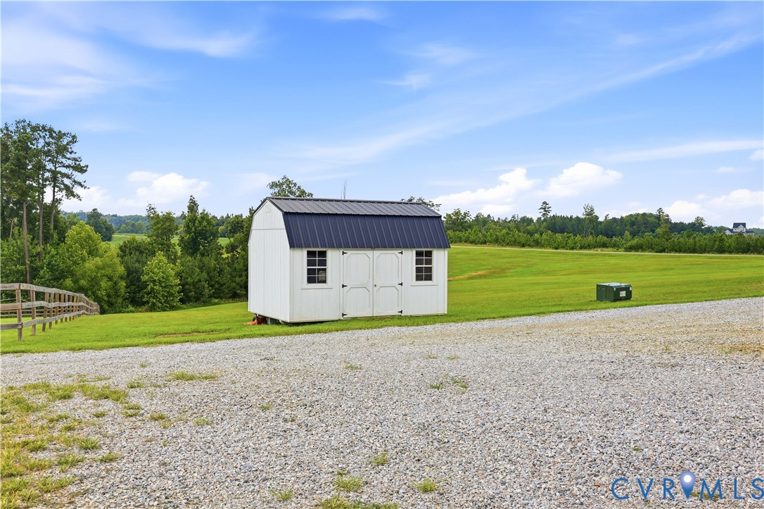 White storage shed featuring a dark metal gambrel roof and two windows