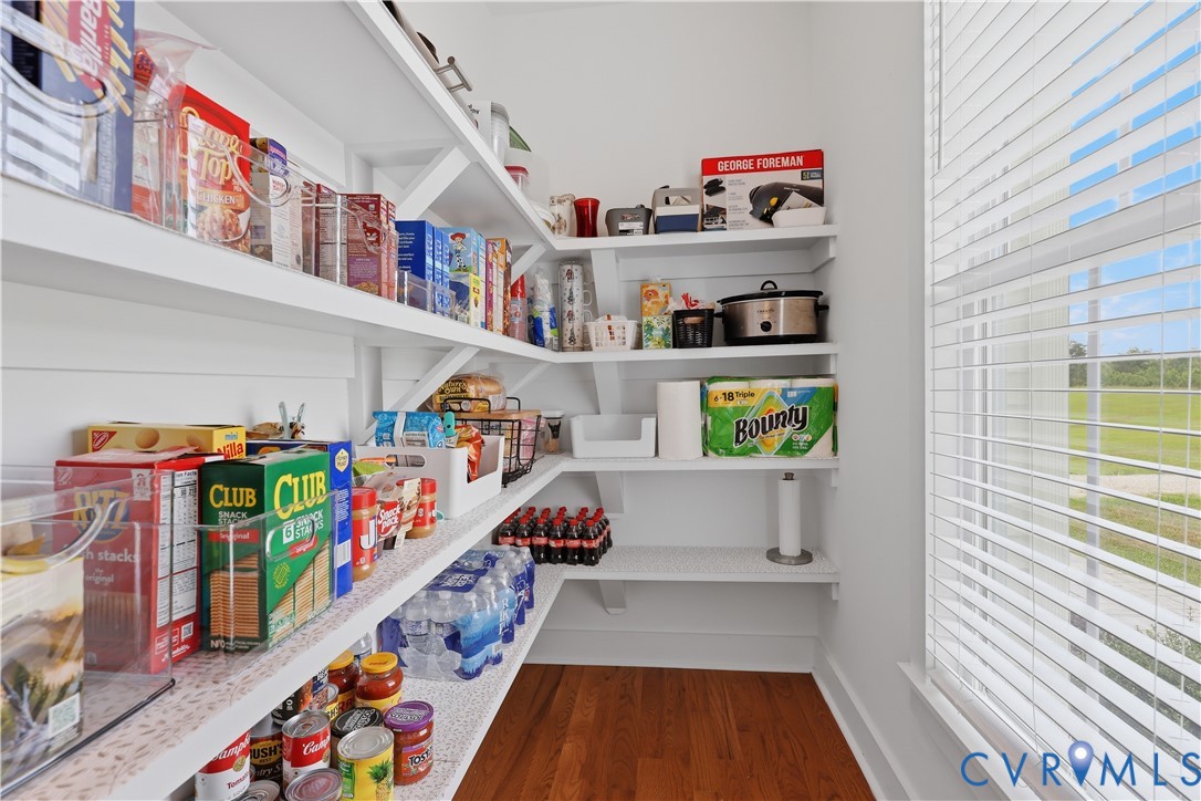Spacious pantry featuring extensive built-in white shelving, wood-finish flooring, and a large window with privacy blinds