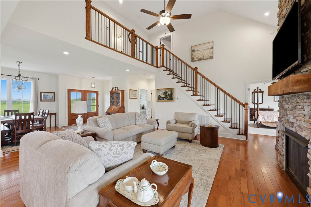 Two-story living area featuring wood-finish flooring, a stone fireplace with a substantial wood mantel, and a prominent staircase with dark wood handrails and black balusters