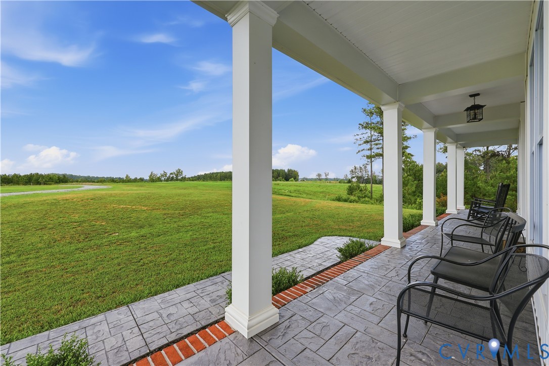 Expansive covered front porch featuring a stamped concrete surface with brick accents, multiple white columns, and a pendant light fixture