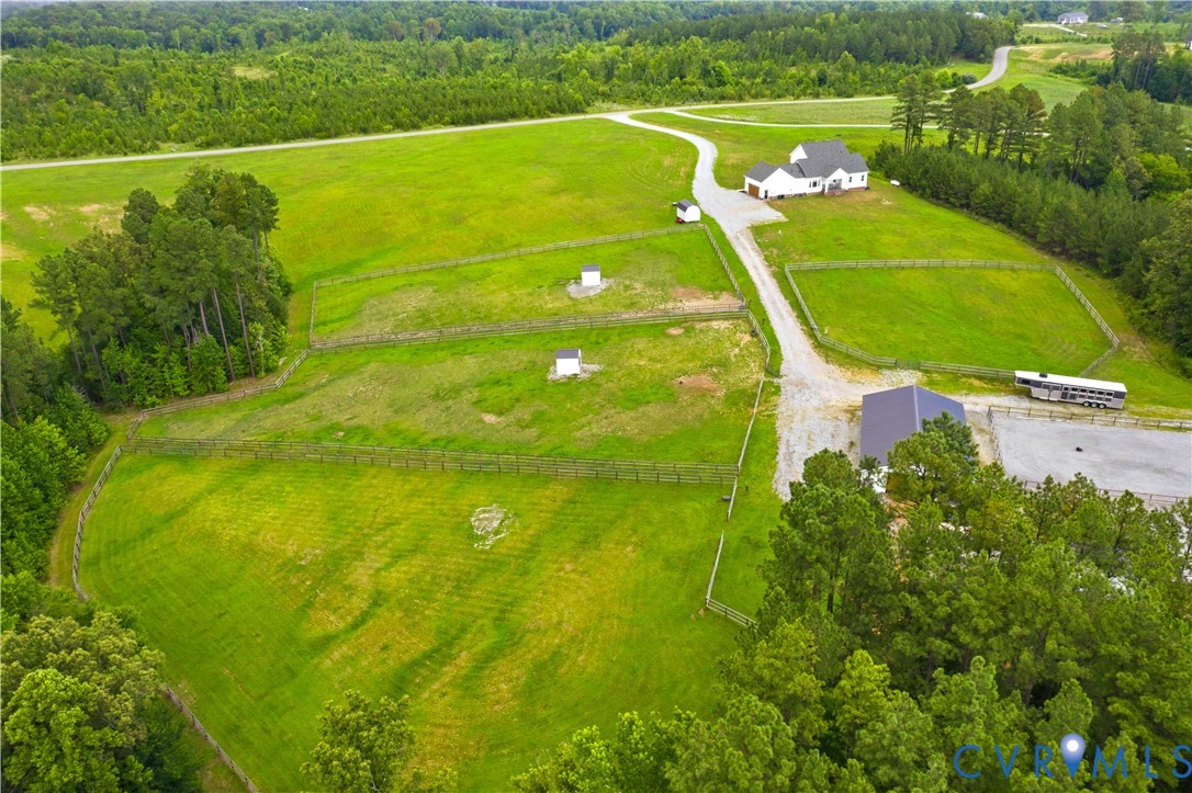 Expansive property featuring a white single-story residence, multiple fenced pastures, a large grey barn, and a gravel drive