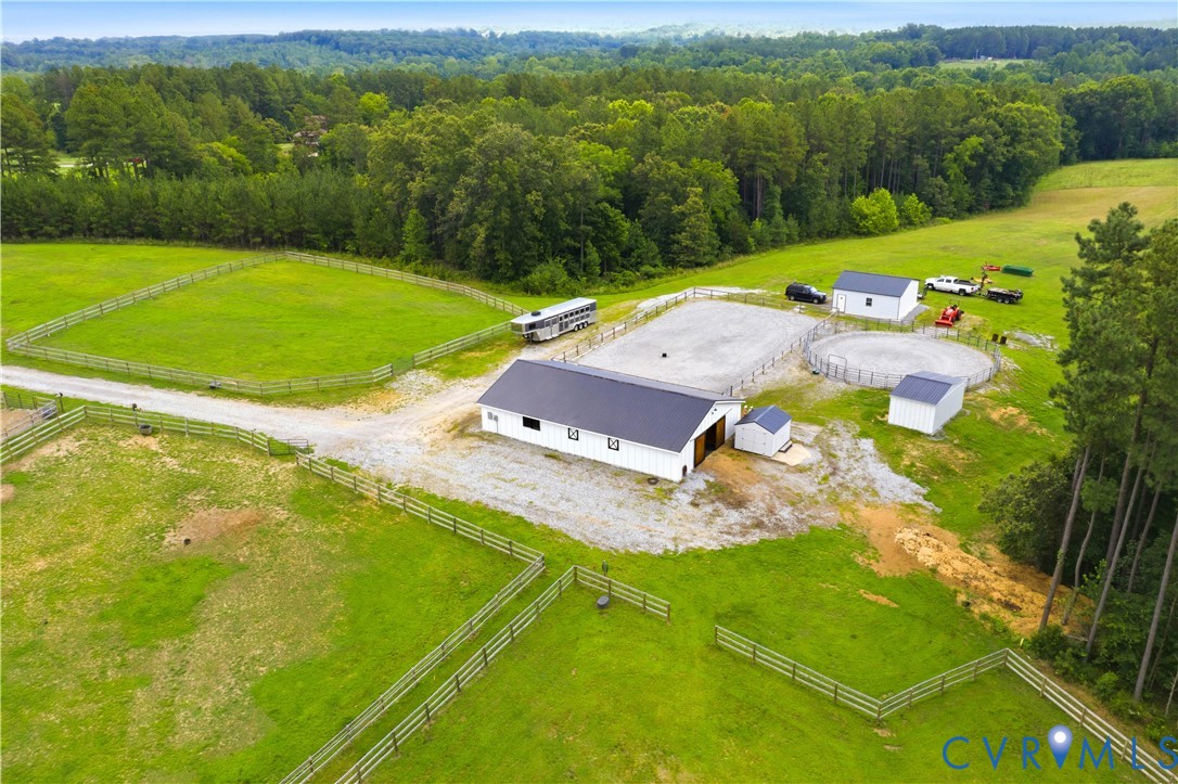 Expansive property featuring a white barn with a dark roof, multiple fenced green pastures, a gravel riding arena, and additional outbuildings, all surrounded by mature treelines