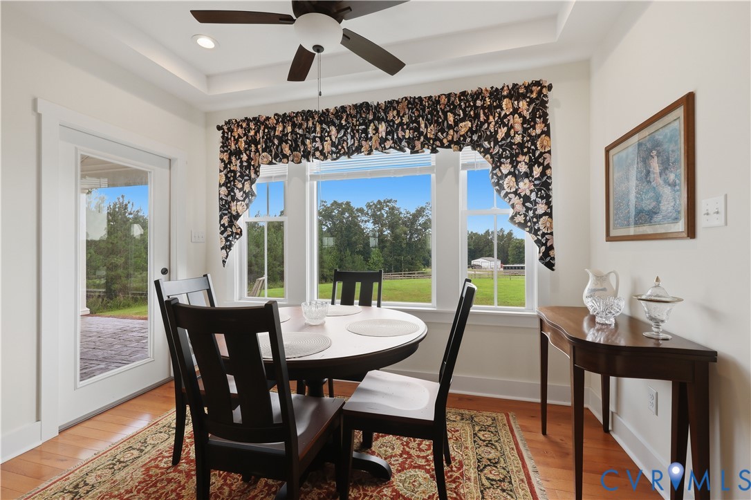 Dining space featuring wood-finish flooring, a tray ceiling with recessed lighting, and a ceiling fan
