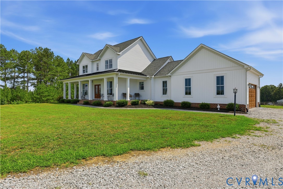 White two-story home with a wide covered front porch, a gravel driveway, and an attached garage featuring a wood-panel door