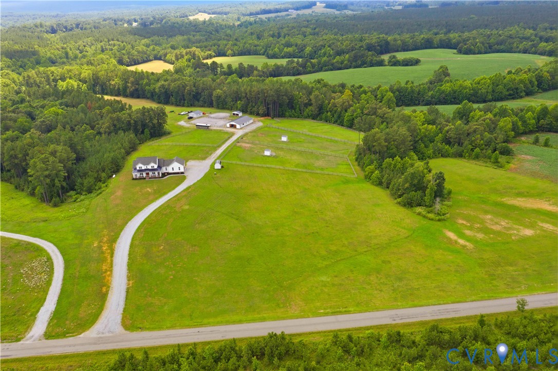 Expansive property featuring a white residence with a dark roof and a porch, surrounded by lush green fields and mature trees
