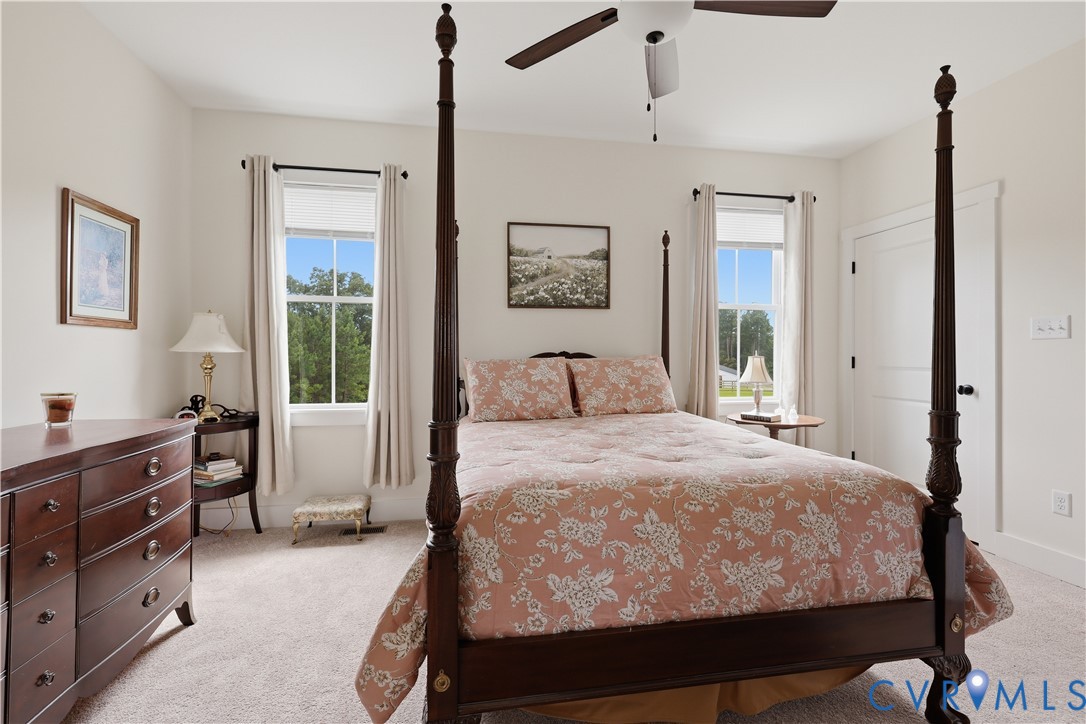 Bright room featuring neutral wall paint, carpet flooring, a ceiling fan, and two windows