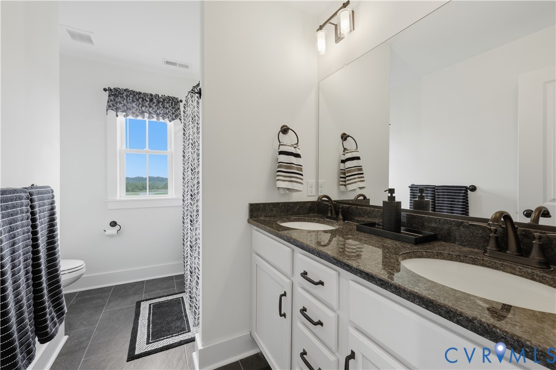 Double vanity with dark stone countertop, white cabinetry, and brushed bronze fixtures