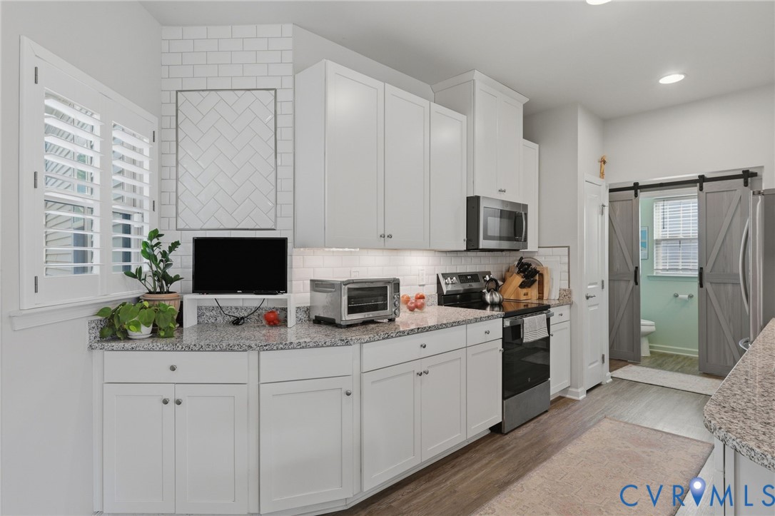 Kitchen featuring white cabinetry, speckled countertops, stainless steel appliances, and a subway tile backsplash