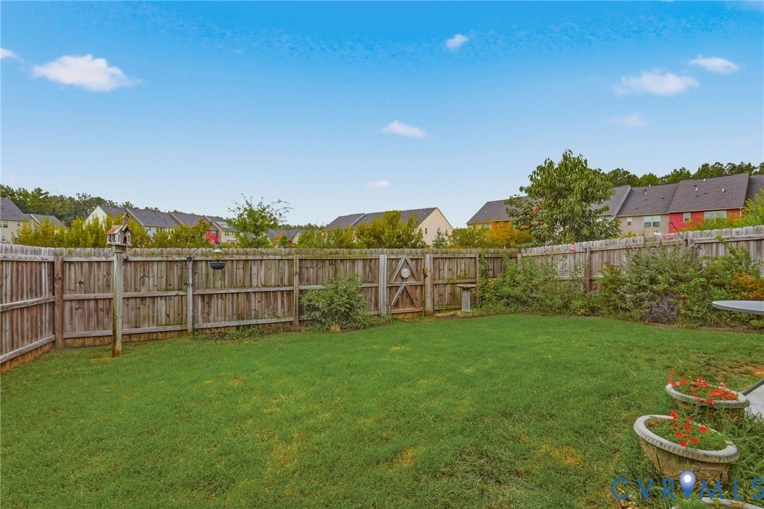 Expansive lawn area enclosed by a wooden privacy fence, featuring a wooden gate and established perimeter shrubs