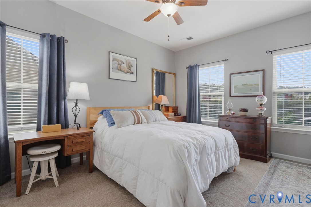 Carpeted room featuring a ceiling fan with integrated lighting, multiple windows with blinds, and neutral wall tones