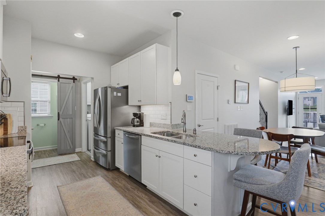 Modern kitchen featuring a large island with a stone countertop, white shaker cabinetry, stainless steel appliances, and wood-finish flooring