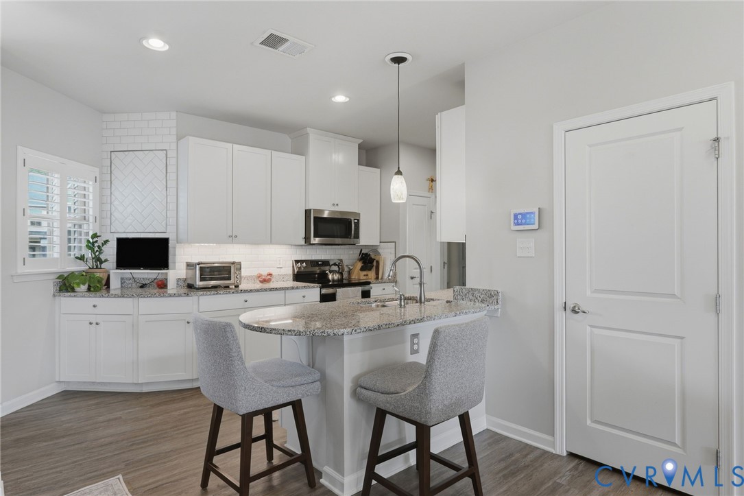 Contemporary kitchen featuring white cabinetry, wood-finish flooring, recessed lighting, and a granite island with a built-in sink