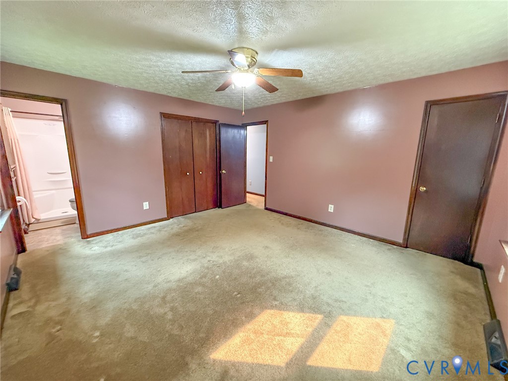 Carpeted interior room featuring a ceiling fan with light fixture, wood-finish doors, and a partial view of a white shower stall