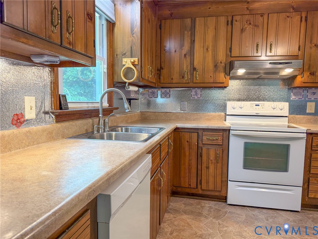 Kitchen featuring wood cabinetry, laminate countertops, a double basin stainless steel sink with a gooseneck faucet, a white electric range, and a white dishwasher