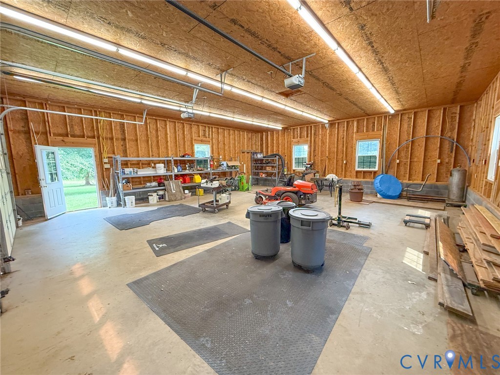 Spacious garage featuring exposed wood framing, concrete flooring, multiple windows, and a side entry door