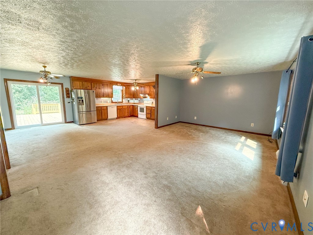 Open-concept living area featuring a kitchen with wood cabinetry, stainless steel refrigerator, and white appliances